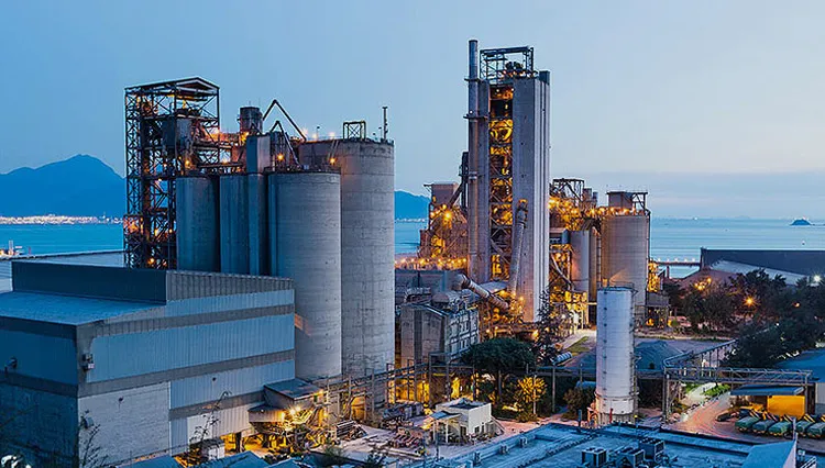 A large industrial processing plant lit up at dusk, with silos and steel gantries against a coastline.